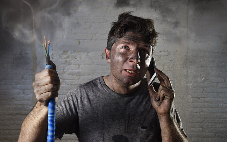 Man covered in soot holding damaged wiring after a failed electrical repair